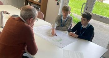 Students Alex and Matt sat opposite a staff member looking at plans and maps 