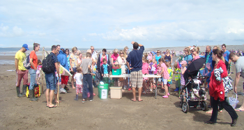 Group of children and their families gathering round a table on the beach to listen to the ranger before undertaking the activity. 