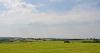 DCA 36: Far reaching view southwards from Staddon Moor over pasture fields, and the caravan park and large storage building at Headons Farm (beyond which there are wind turbines), towards Bodmin Moor in the distance.