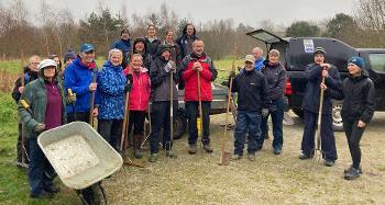 Photo of a group of volunteers, holding wheelbarrows, shovels and rakes