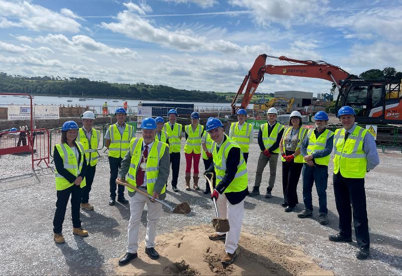 Picture of various people involved with the project, all wearing hi-vis and hard hats, breaking the ground on site
