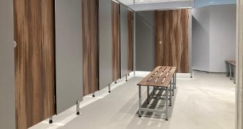 Photo of new changing rooms in the leisure centre, showing new cubicles with dark wooden effect doors and a matching bench in the middle of the room. 