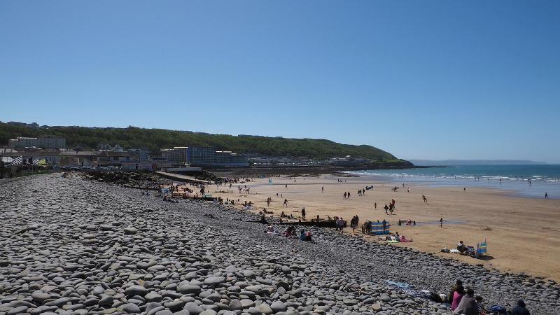 Image of the pebbleridge along Westward Ho! beach, showing the pebbles on the left and the beach with people and the sea on the right.