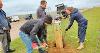 Photo of volunteers and rangers helping to place a new wooden signpost in the ground. They are refilling the hole with soil. 