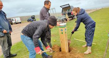 Photo of volunteers and rangers helping to place a new wooden signpost in the ground. They are refilling the hole with soil. 