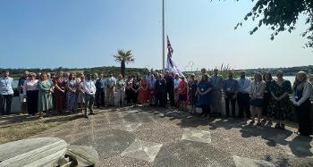 Group photo of multiple Torridge Councillors and Officers, stood at the flagpole of Riverbnak House to commemorate VJ Day
