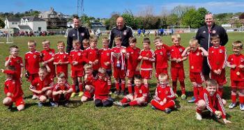 Photo of a football team from Bideford AFC, consisting of children wearing red football shirts and holding a trophy. 