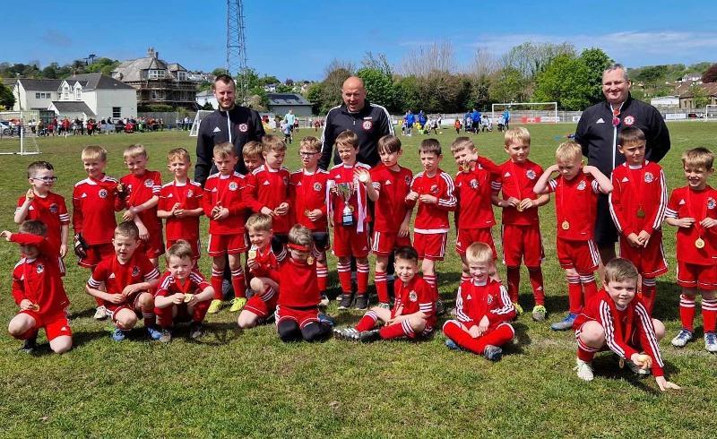 Photo of a football team from Bideford AFC, consisting of children wearing red football shirts and holding a trophy. 