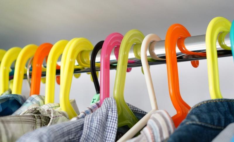Picture of the tops of multiple coloured clothes hangers, hanging on a clothes rail.