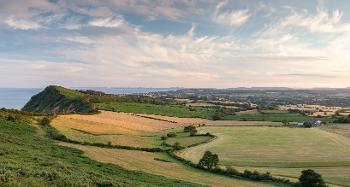 Scenic view across fields with cloudy blue sky