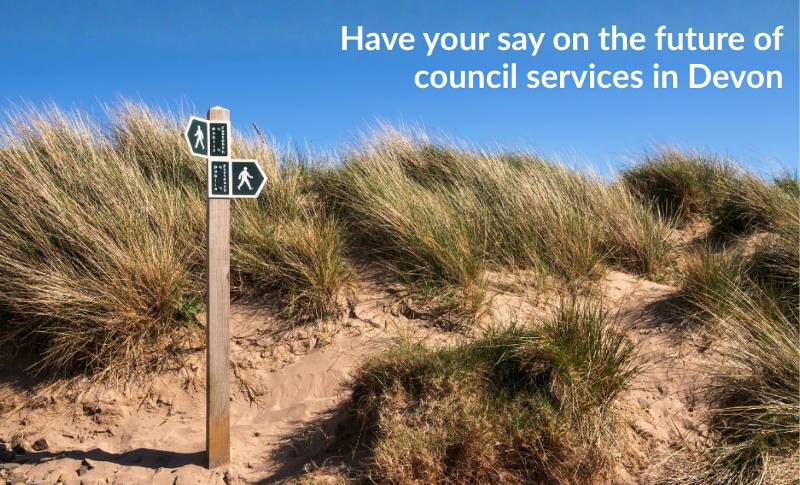 A photo of a walking path sign on some sandy dunes with the text 'have your say on the future of council services in Devon' across the blue sky. 