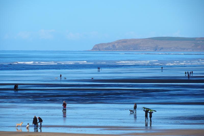 A photo of Westward Ho! beach with blue sky and blue waters, a variety of people on the beach